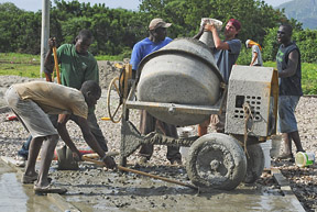 Volunteers work with the head concrete team in the village to finish pouring the basketball court.