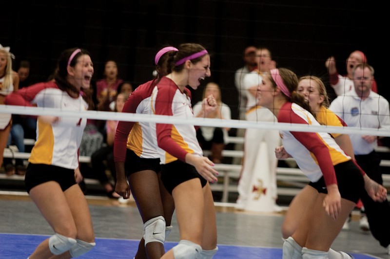 Members of the ISU volleyball team celebrate after a score against Texas A&M during Saturdays game at Ames High School. The Cyclones participated in a pink out by wearing pink hair wraps.