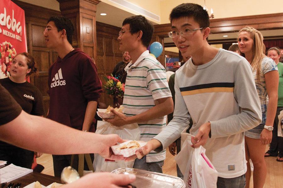 Tang Xiao Duan, graduate student in mechanical engineering, takes a box of chips and queso from Jeffery Nauditt, freshman in construction engineering at the Qdoba booth during Welcome Fest on Wednesday, Aug. 25. in the Great Hall of the Memorial Union