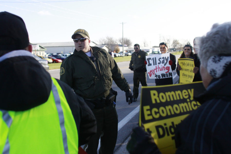 A police officer reminds the people protesting across the street from Mitt Romneys event to stay safe and off the roadway Friday, Oct. 26, at Kinzler Construction Services in Ames. Some of the protesters stood outside of the event dressed as Mitt Romney.
