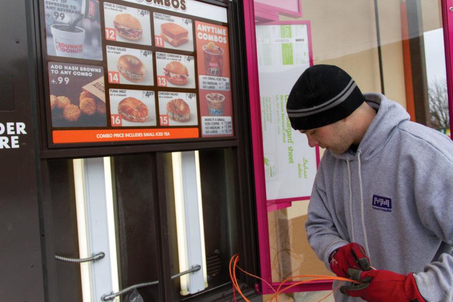 Justin Ross installs new electronics on the outdoor menu sign at the new Dunkin Donuts. Dunkin Donuts will be opening in Ames on Feb. 20.
