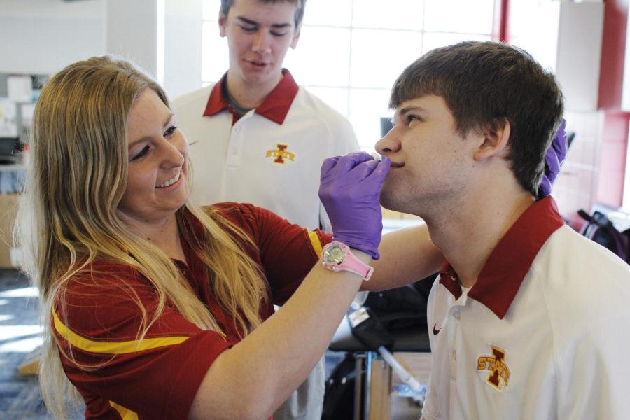 Kayla Kleihauer (left), graduate student in education and athletic trainer, demonstrates the procedure to fix a bloody nose on Eric Bornholdt (right), junior in athletic training, while Billy Lutz (center), junior in athletic training, aids Kleihauer by applying the skin lube to the nose plug Feb. 12 at Lied Recreation Center. These three athletic trainers will attend the state of Iowas wrestling tournament in downtown Des Moines and will aid wrestlers who need medical treatment, ranging from concussions to a bloody nose.
