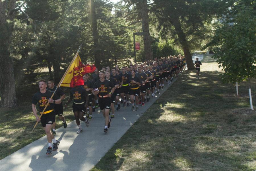 The ISU Army ROTC program runs through campus in front of Catt Hall while carrying the Cy-Hawk game ball for Saturday.