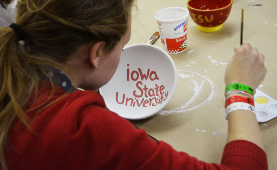 An ISU family member shows Cyclone spirit by painting Iowa State University in her pottery.
