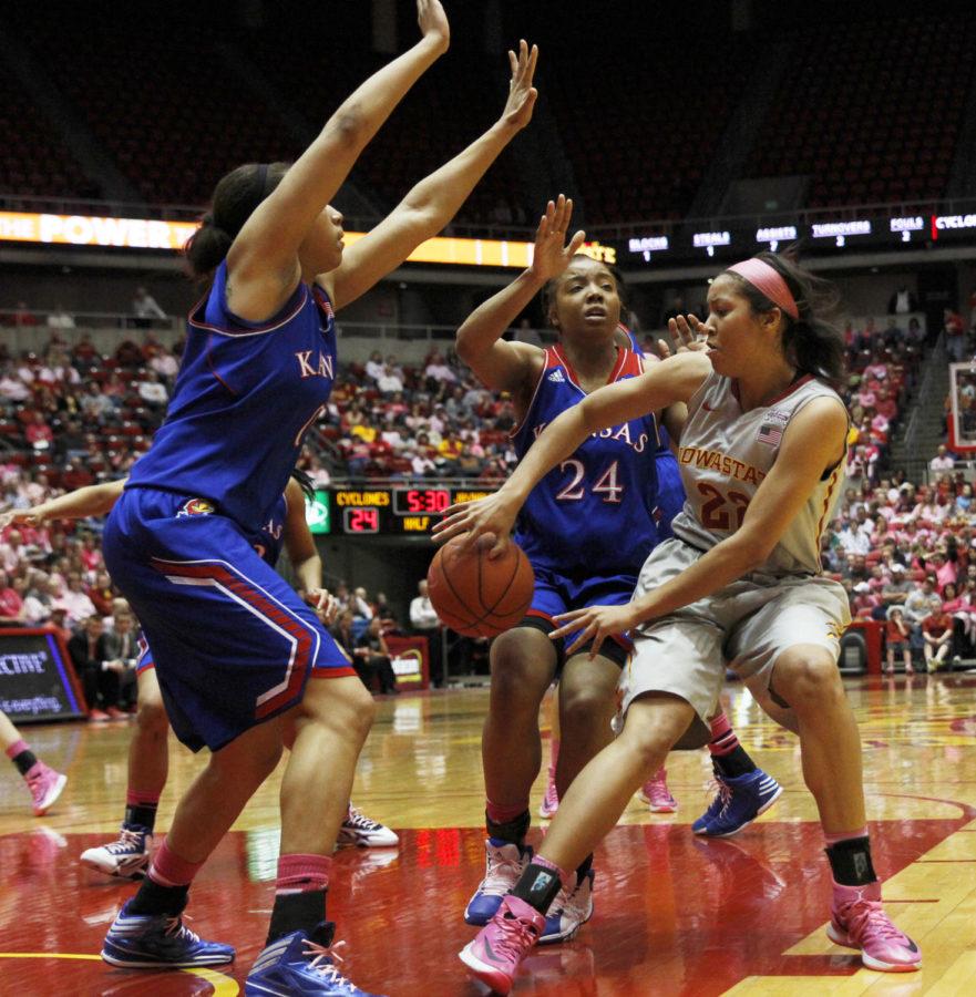 Junior guard Brynn Williamson passes the ball between two Kansas defenders on Feb. 15 at Hilton Coliseum. Williamson ended the game with one assist and two points in the 72-69 victory.