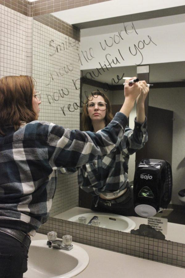 Brianna Burgert, senior in mechanical engineering, writes Smile, show the world how beautiful you really are, on a bathroom mirror on campus. The Sninja Club regularly goes on smile missions to help others feel good about themselves.