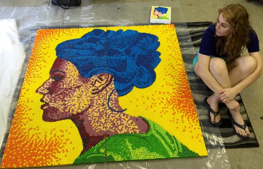 Caroline Freese, senior in Integrated Studio Arts, sits next to her completed self-portrait composed entirely out of Skittles.