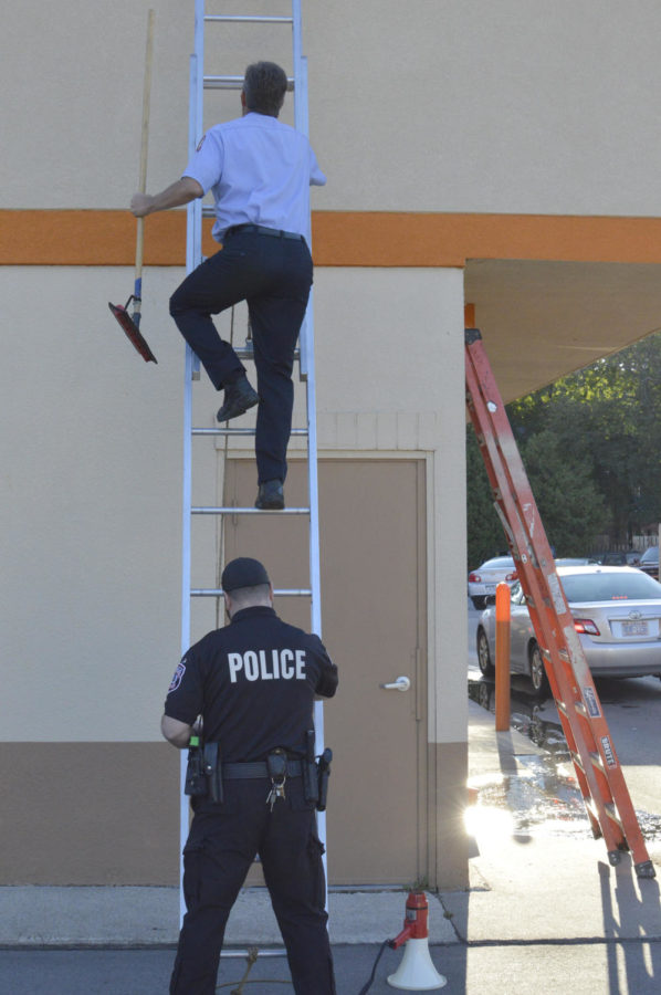 Officer Nick Grossman holds a ladder for a firefighter outside of Dunkin Donuts on Sept. 18. The ISU Police Department handed out vouchers for free coffee in exchange for donations toward the Special Olympics and the Fire Department cleared the rooftop of excess water.