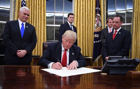 President Donald Trump signs a document on the Resolute Desk in the Oval Office.