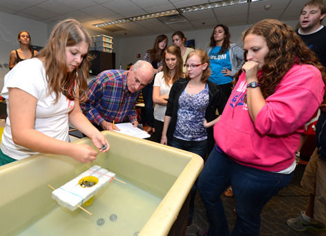 Larry Genalo looks on as future teachers watch a demonstration about an activity to teach young students about mass, weight, volume and water displacement.