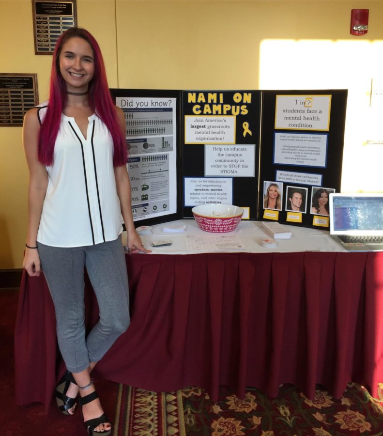 Leah+Beman+stands+in+front+of+a+NAMI+display.+NAMI+is+a+student+organization+aimed+at+helping+promote+mental+health.