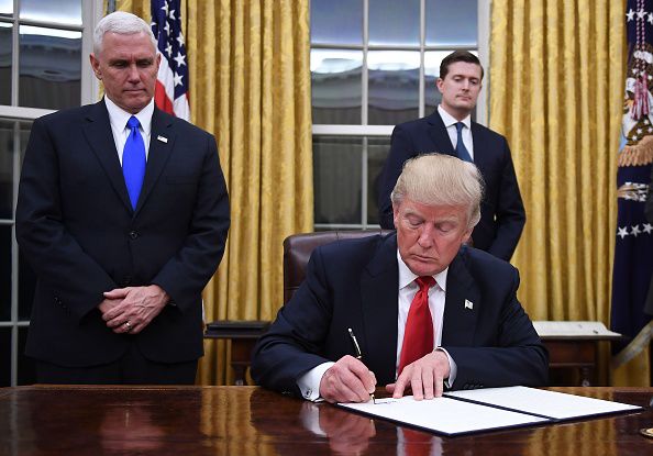 US President Donald Trump signs an executive order as Vice President Mike Pence looks on at the White House in Washington, DC on January 20, 2017. 