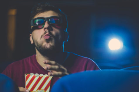 Man eating popcorn in the movie theater while watching a serious movie.