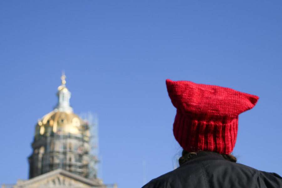 A woman wearing a red pussy hat listens to speakers at the second annual Womens March at the State Capitol building in Des Moines on Jan. 20, 2018.