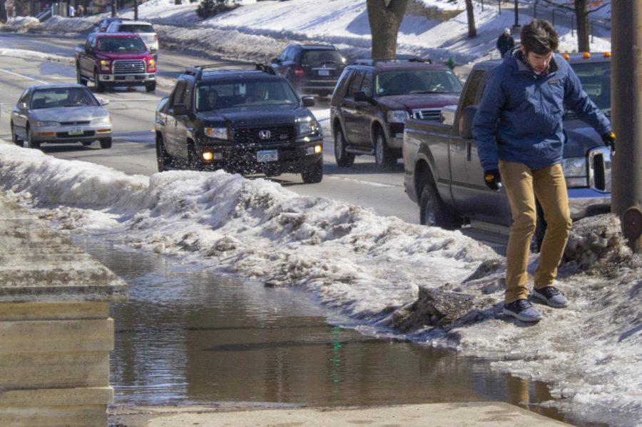 Freshman in software engineering Matthew Medley avoids the flooded sidewalk in front of the Memorial Union on Lincoln Way on Sunday. Warmer temperatures, rainfall and the melting snow are causing flooding in certain parts of Ames.