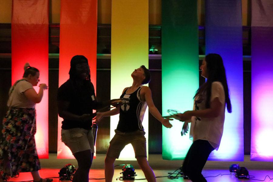 LGBTQIA+ Community Welcome attendees Mahogani Willis, Jolene Bowman and Ankita Budhathoki dance in front of a large hanging Pride flag Aug. 27 in the Great Hall of the Memorial Union. 