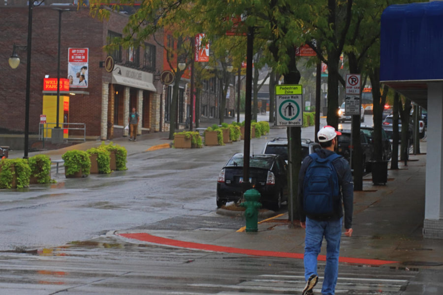 Student calmly walking across Lincoln Way and Welch Avenue from campus during a small rain storm.