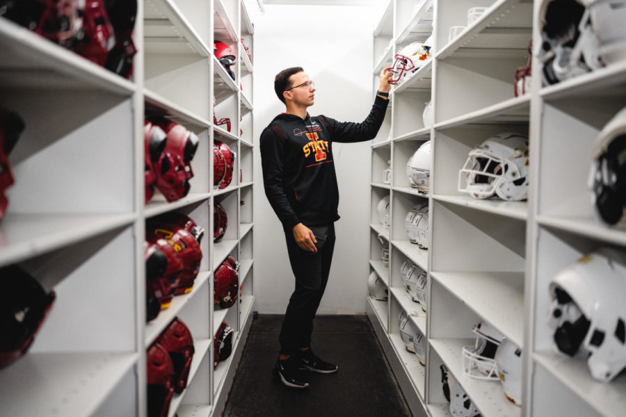 Austin Breitbach picks out his favorite color combination of football helmet off of the electronic storage shelves at the ISU equipment facility. Dec. 7, 2022. 