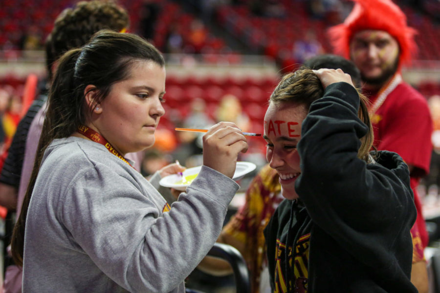 Brooke Rogers 25 (left) paints a student section members face before the Cyclones game against K-State on Jan. 24. Being apart of Hilton Magic is really amazing, you just feel so electric as soon as you come in here, Rogers said.