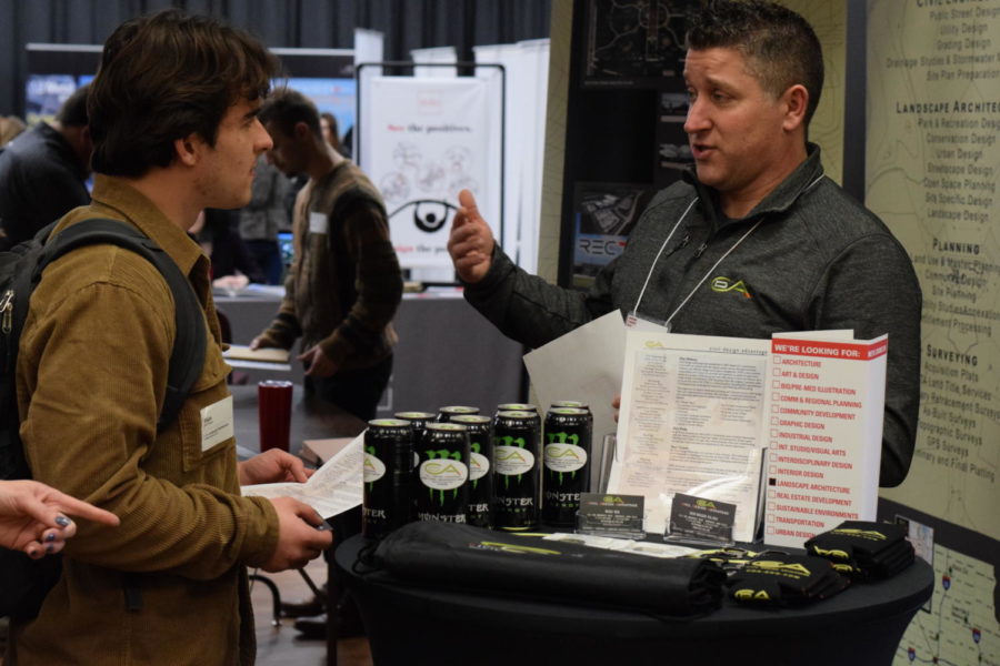 Many booths at the career fair offered a variety of snacks and goods to give away to interested students. Pictured is Elijah Wagner, a junior in landscape architecture, talking with a representative of Civil Design Advantage before partaking in the Monster Energy Drinks set out on the table.