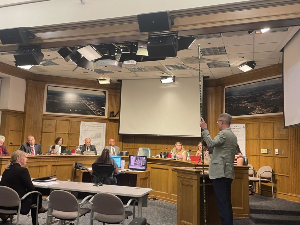 Ames resident Dylan Kline demonstrates to the Ames City Council what a ten-foot vegetation clearance would look like using measuring tape.