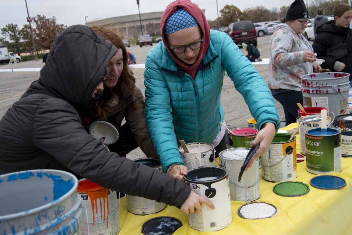 Members of different clubs and organizations crack open cans of paint during The Painting of Victory Lane event at the beginning of Iowa State’s Homecoming week on Sunday, Oct. 29, 2023, outside the Alumni Center in Ames, Iowa.