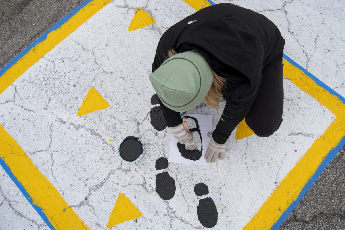 Andralynne Piittmann, a member of the Criminal Justice Club, uses a stencil of a footprint to paint her club’s square during The Painting of Victory Lane event at the beginning of Iowa State’s Homecoming week on Sunday, Oct. 29, 2023, outside the Alumni Center in Ames, Iowa.
