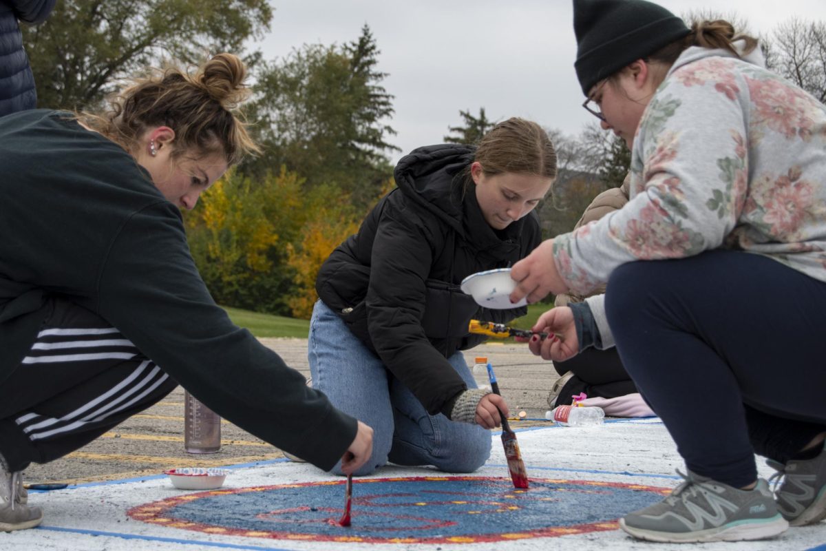 President of the Honors Student Board Julia Litecky, left, and members Hope Nolan, middle, and Frances Jackson, right, paint their square during The Painting of Victory Lane event at the beginning of Iowa State’s Homecoming week on Sunday, Oct. 29, 2023, outside the Alumni Center in Ames, Iowa.
