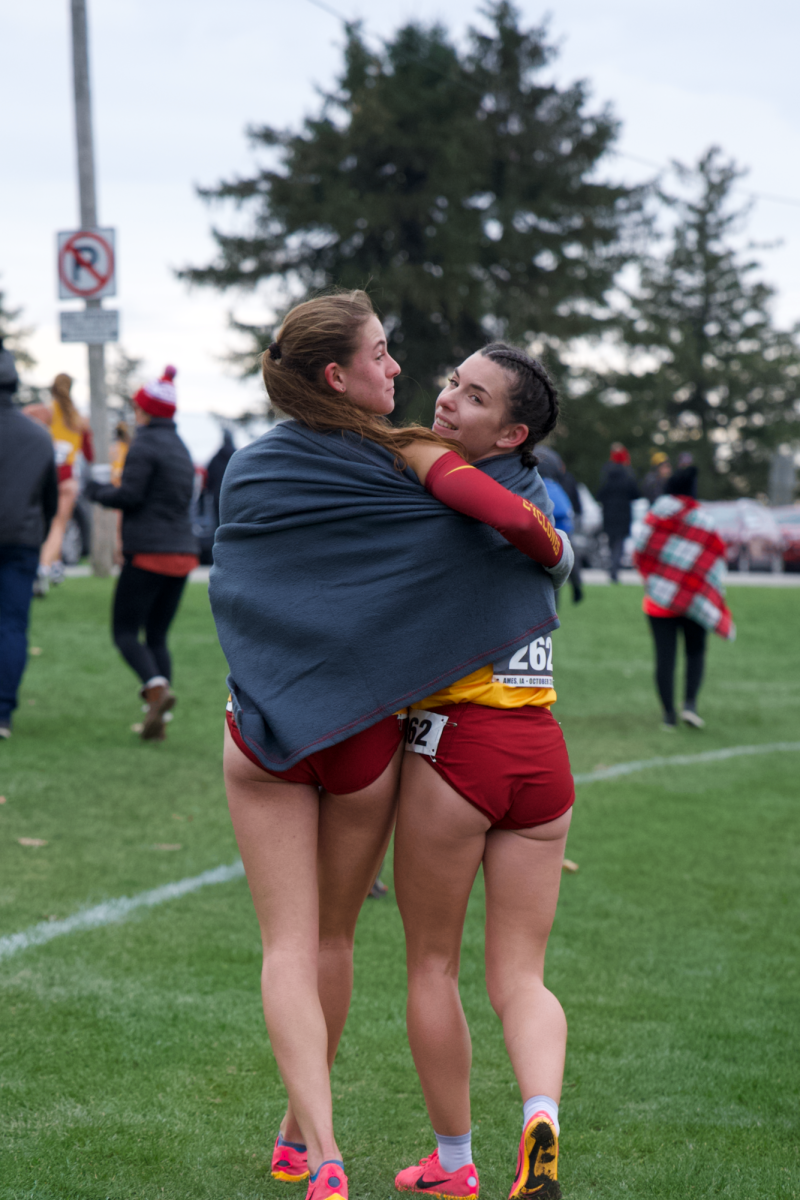 Sheridan Wheeler (Left) and Maelle Porcher (Right) share a blanket to escape the cold October morning during the Big 12 Championship race on Oct. 28, 2023 in Ames, Iowa.