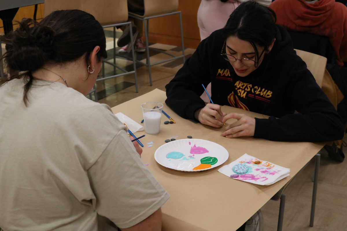 Victoria Brewster (in black) and Makena Vician (in white) painting kindness rocks at an event held by Mindspace in the Hamilton commons on Nov. 29, 2023. 