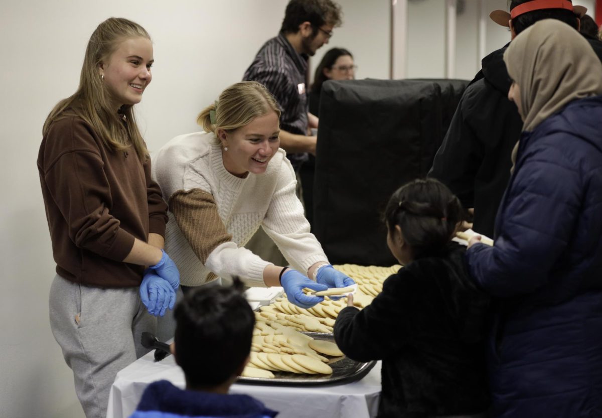 Reagan Duwe, left, and Lauren Kennedy, right, pass out cookies to a family attending Winterfest in the Memorial Union on Friday, Dec. 1, 2023. Attendees could decorate cookies for free in the MU Commons. 