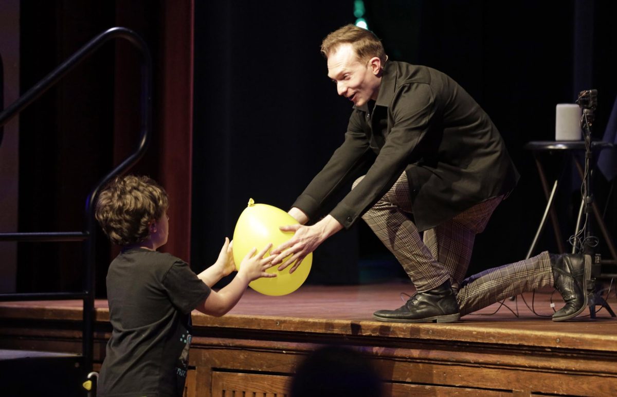 Magician Trigg Watson performs a trick with an audience member during his show in the Memorial Union Great Hall during Winterfest on Friday, Dec. 1, 2023. Watson later made the balloon pop as he stood across the stage. 