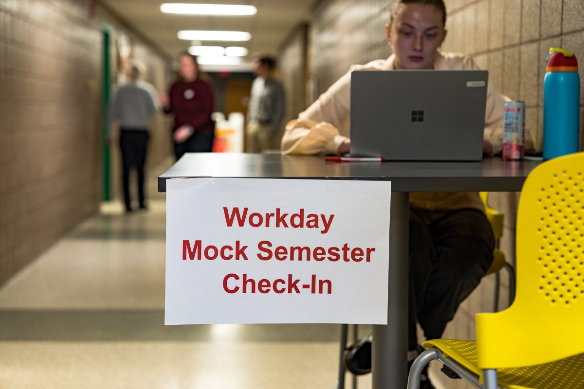 Madisyn Postma sits at a high top table checking in individuals for the Workday Mock Semester in Durham Hall on Feb. 1, 2024.