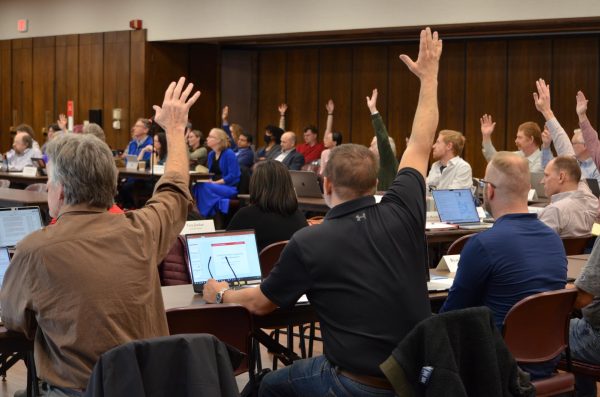 Members of the Faculty Senate raise their hands for a vote during the meeting in the Memorial Union Sun Room on March 19, 2024.