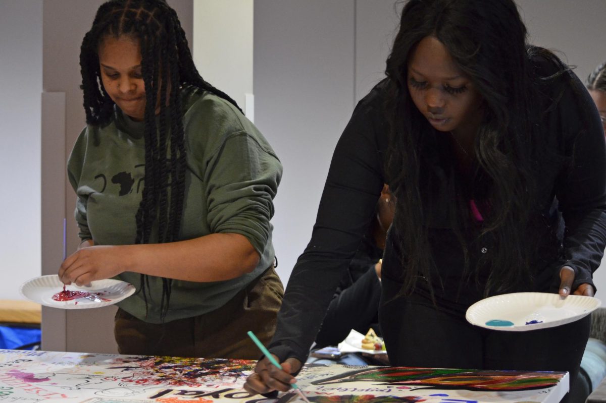 Brya Poindexter (left) and Priscilla Timothy (right) paint on the collaborative art piece in the Memorial Union Multicultural Center during the Third Annual Black Art Exhibit on Thursday, March 28, 2024.