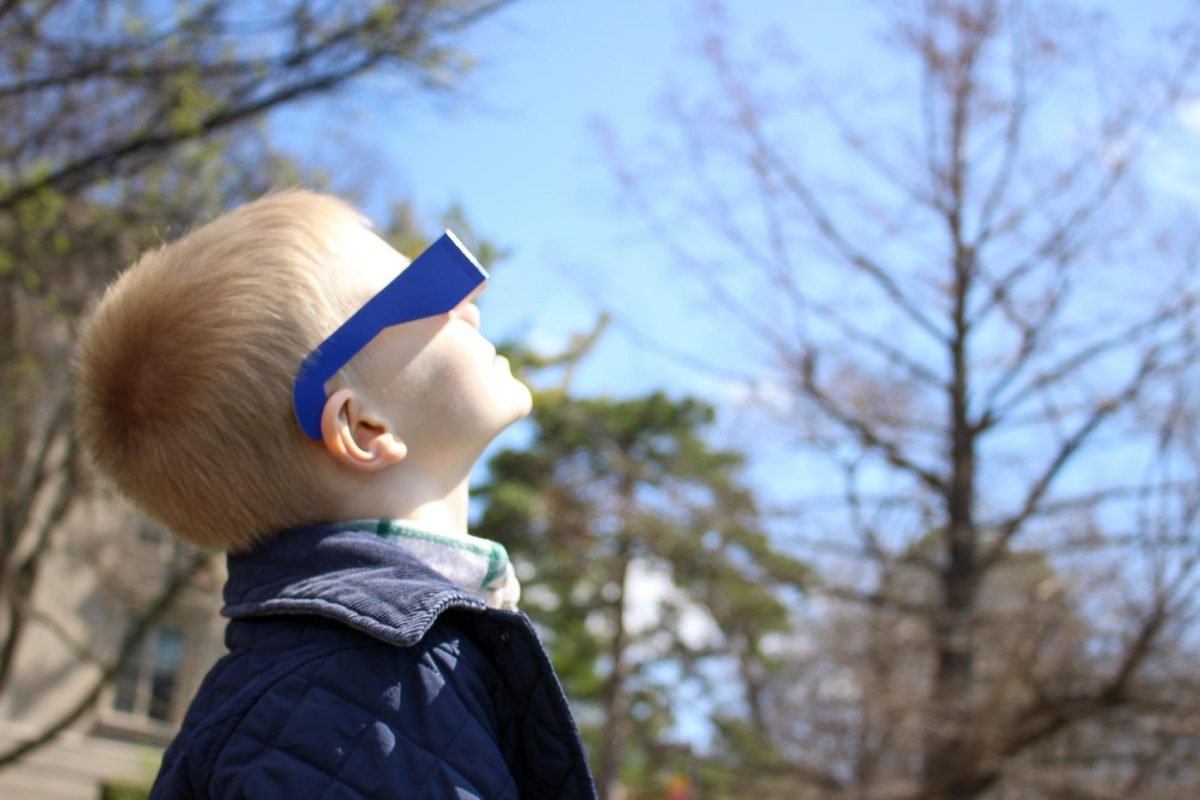 A young boy (Stefan) watches the eclipse with his family, including his father Evgeny Chukharev. Iowa State University central campus, April 8th 2024.