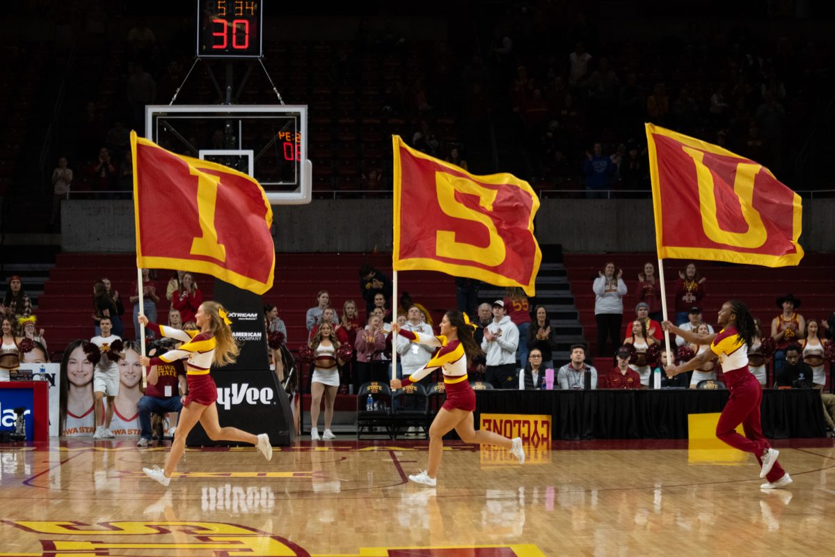 The cheer team runs on the court with "ISU" flags, Hilton Coliseum, Ames, Iowa, Dec. 15, 2024. 