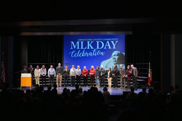 Speakers and award recipients stand together on stage and sing "We Shall Overcome" at the end of the Ames/Story County Community MLK Day 2025 Celebration, Ames City Hall Auditorium, Jan. 20, 2025.